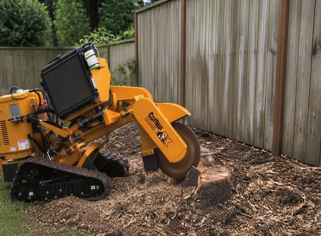 Tracked stump grinder grinding a tree stump beside a timber fence