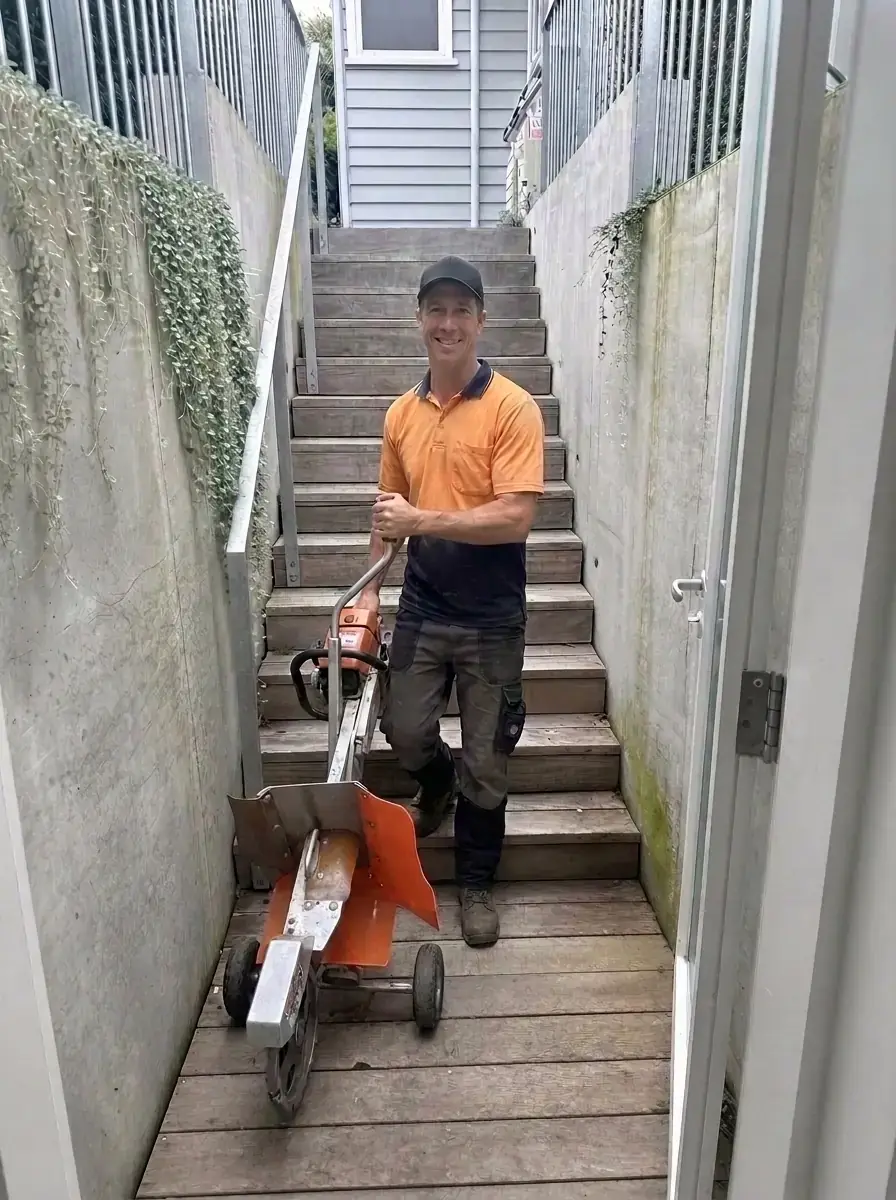 Operator carrying a portable stump grinder down narrow outdoor steps